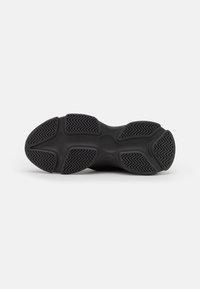 Black athletic shoe sole with a textured rubber pattern, featuring deep grooves and ridges for traction and stability.
