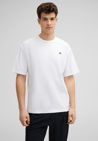 Witte korte mouwen t-shirt met een ronde halslijn, voorzien van een klein zwart logodetail op de borst. Gemaakt van zachte, gladde stof.