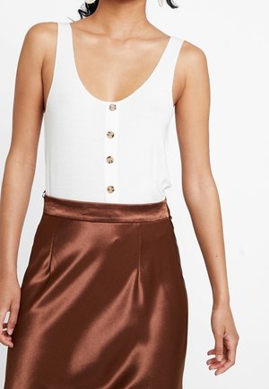 Débardeur blanc à côtes avec un décolleté plongeant et cinq boutons beige sur le devant, associé à une jupe en satin brun brillant.
