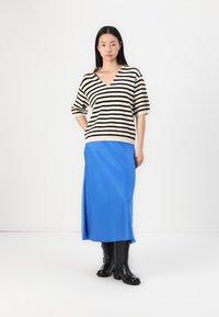Pull rayé beige et noir avec un col en V, associé à une jupe midi bleue et des bottes noires jusqu'aux genoux. Tissu lisse ; coupe décontractée.