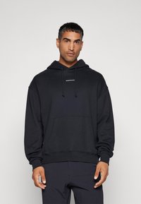 Svart hettegensere laget av myk stoff, med kengurulomme, justerbar snorhette og minimalistisk logo på brystet.