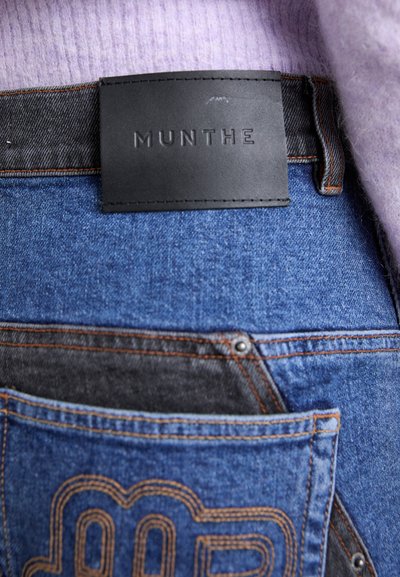 Denim teksad, millel on mustast nahast brändi sildiga, oranž õmblus ja tagakotil unikaalsed tikandid.