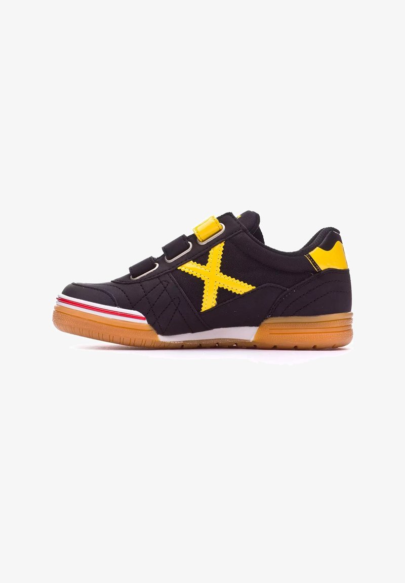 Zapato deportivo negro con un acento amarillo, que presenta un gran logo amarillo en forma de 'X', tres tiras de Velcro y una suela de goma con rayas rojas.