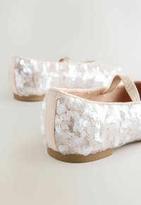 Ballerinas in hellem Beige, bedeckt mit schillernden Pailletten, mit einem weichen Innenfutter, flacher Sohle und einem dünnen, glitzernden Riemen.