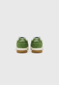 Zelene antilop cipele s bijelim akcentima i potplatom od gume, s "new balance" marketingom na peti. Dizajn s okruglim prstima.