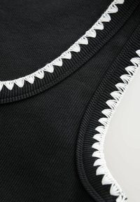 Tissu noir côtelé avec gros plan sur les bords présentant un détail de couture en boucle triangulaire blanche sur un matériau textile.