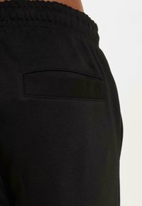 Sorte atletiske joggebukser med en glatt tekstur, med elastisk midjebånd og en bakre lomme. Designet er enkelt og funksjonelt.
