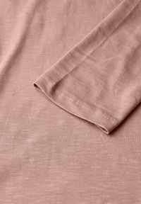 Tejido de algodón de color rosa claro con una textura suave, que presenta un acabado liso y un diseño de canalé simple. El dobladillo de la manga está cosido de manera impecable.