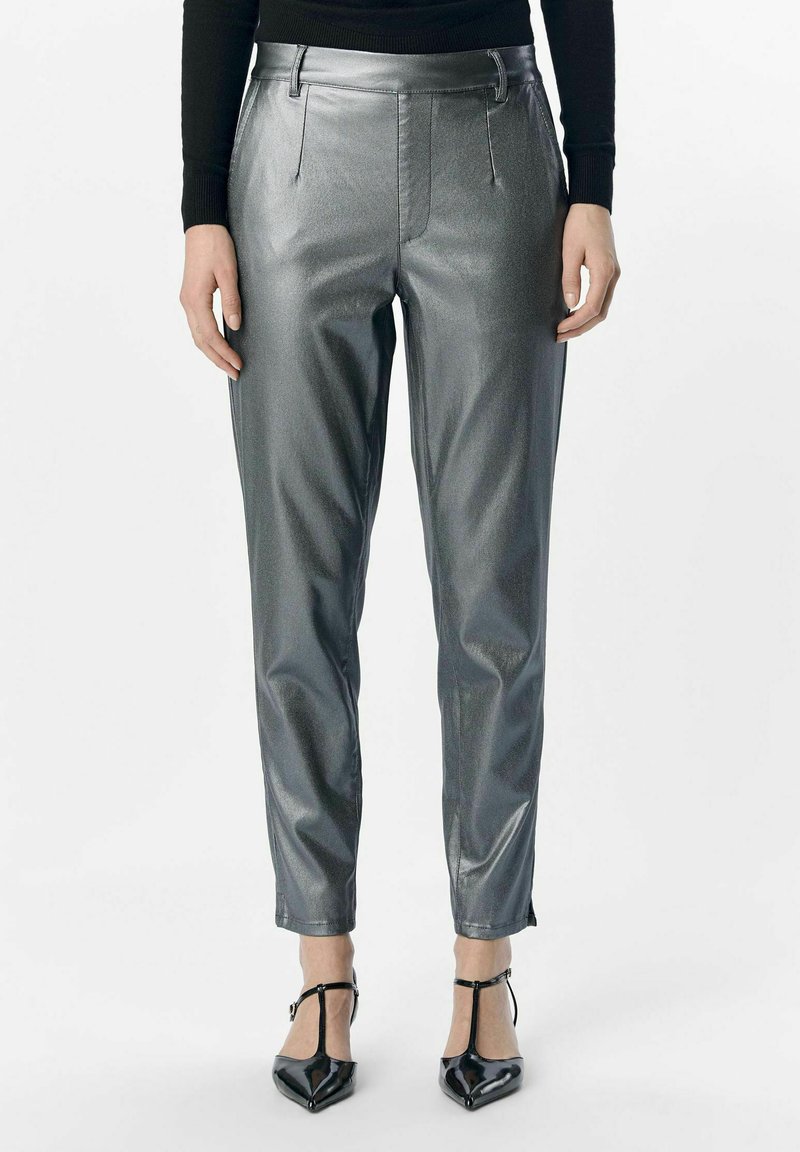 Metallische zilveren broek met een slim fit, een gladde textuur, voorplooien en ritsen bij de enkels. Gekleed met zwarte pumps met een spitse neus.