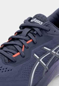 Baskets de sport bleu foncé avec une tige texturée, accent rouge sur les lacets, logo blanc et détails argentés. Dispose d'une maille respirante et d'une semelle rembourrée.