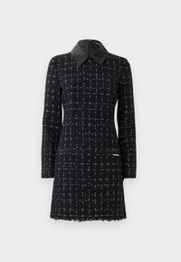 Ein schwarzes Kleid mit texturiertem Rautenmuster, ausgestattet mit einem Lederkragen und zwei vorderen Taschen, für einen modernen Look gestaltet.