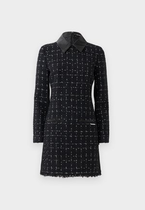Musta mekko, jossa on teksturoitu ruutukuosi, nahkakaulus ja kaksi etutaskua, tyylitelty moderniin ilmeeseen.