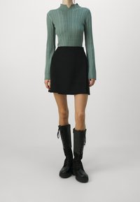 Mátově zelený žebrovaný top s dlouhým rukávem a vysokým límcem; černá sukně s vysokým pasem; černé šněrovací boty po kolena s masivními podrážkami.