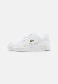 Baskets blanches en cuir synthétique avec une semelle plate, des détails latéraux perforés et un logo Lacoste doré sur le côté extérieur.