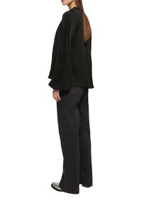 Schwarze, plissierte Bluse mit weiten Ärmeln, kombiniert mit schwarzen, ausgestellten Hosen und schwarzen Schuhen, die eine glatte Textur und ein schichtartiges Design präsentieren.