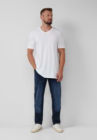 Witte T-shirt met korte mouwen en V-hals, gecombineerd met donkerblauwe jeans en witte sneakers. Eenvoudig ontwerp met een relaxte pasvorm.