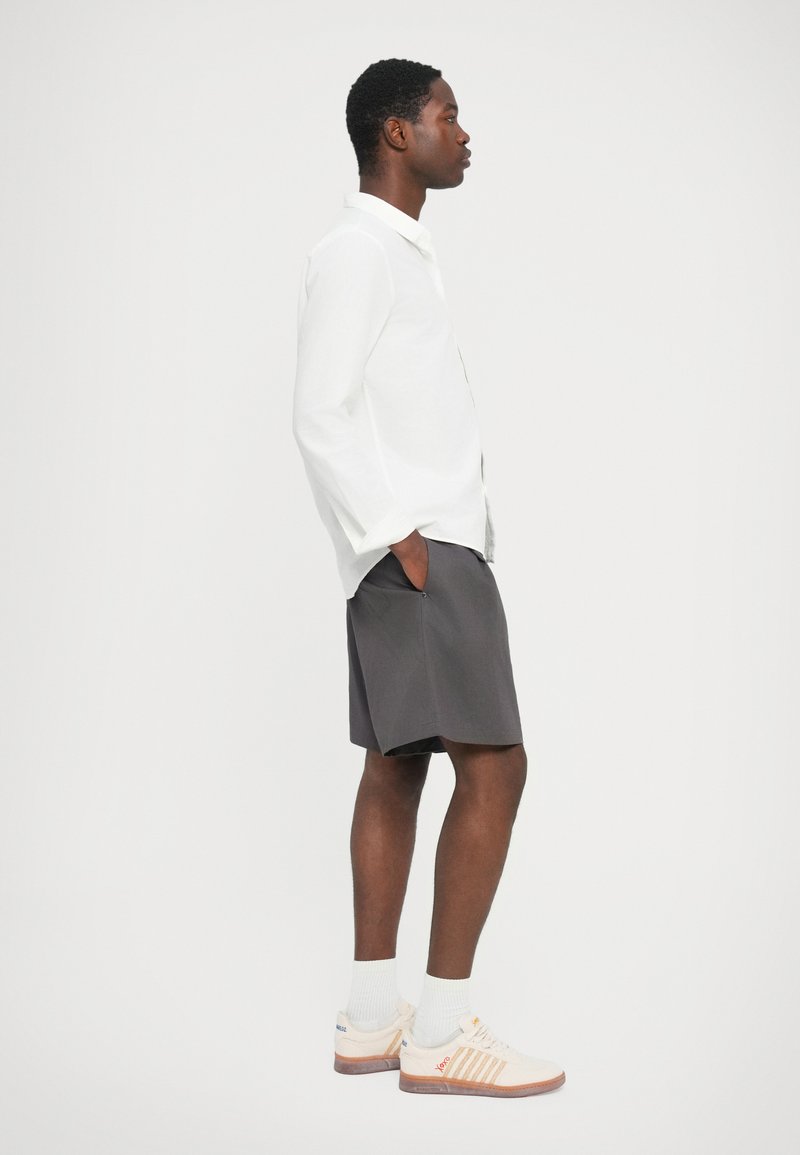 Witte blouse met lange mouwen, grijze shorts en crèmekleurige sneakers met een oranje accent. Rechte pasvorm, casual ontwerp en zichtbare zakken op de shorts.