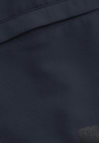 Granatowy materiał o gładkiej teksturze, z widocznym przeszyciem. W pobliżu dolnej krawędzi znajduje się mała etykieta z napisem "KOLOR".