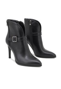 Botas negras de cuero hasta el tobillo con punta estrecha y tacón de 4 pulgadas. Cuentan con cierre lateral de cremallera y una correa decorativa con hebilla. Textura suave.