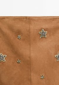 Tissu en suede marron avec des embellissements décoratifs en forme d'étoile en or et en argent, sur une surface lisse avec des coutures visibles.