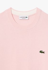 Svetlo roza bombažna majica s ribastim krojem in majhnim zelenim logotipom krokodila Lacoste na prsih. Oblika v rednem kroju.