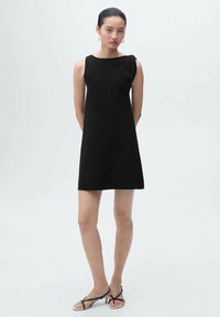 Black sleeveless dress with a structured bodice, featuring a single twisted accent on the shoulder; smooth fabric, straight cut, above-knee length.