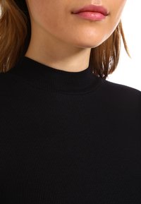 Top noir à col roulé côtelé avec un col haut et une texture subtile, raccourci jusqu'à la clavicule avec un design ajusté.