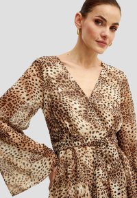 Vestito avvolgente a stampa leopardata in tessuto leggero e trasparente. Presenta un profondo scollo a V, maniche lunghe a campana e una vita regolabile per una silhouette aderente.