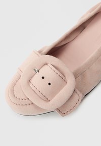 Sapato plano de camurça rosa com bico arredondado, apresentando uma tira larga e detalhe de fivela retangular. Textura suave e acabamentos com costura mínima.