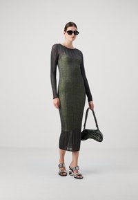 Abito a maniche lunghe con design a coste in verde e nero; silhouette aderente con una texture semi-trasparente. Completato da sandali argentati e una borsa.