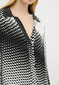 Black and white patterned blouse with a collar, featuring a gradient dot design, lightweight fabric, and front button closure.