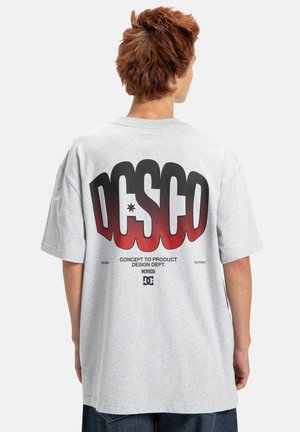 Lichtgrijs oversized T-shirt met een grote rode en zwarte grafiek op de achterkant met "DC" logo en tekst. Korte mouwen, gemaakt van katoen.