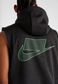Bez rękawów, szary kaptur. Z tyłu znajduje się duże logo Nike z zielonymi kropkami. Kaptur o gładkiej fakturze.