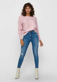 Un pull en tricot rose clair à coupe décontractée, associé à un jean skinny bleu déchiré taille haute et des bottines crème. 