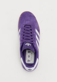 Sapatilhas de camurça roxa com riscas brancas, biqueira arredondada, língua almofadada e sola de borracha natural. Apresenta marcas na língua e na palmilha.