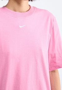 Růžové bavlněné tričko s kulatým výstřihem a krátkými rukávy. Na přední straně je malé bílé logo Nike vyšívané na hrudi.