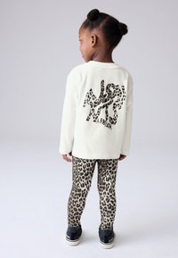 Top blanco de manga larga con un gráfico de estampado de leopardo negro en la espalda, combinado con leggings de estampado de leopardo marrón y zapatillas negras.
