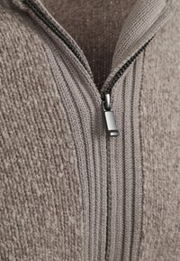 Close-up of a beige knitted sweater with a partially zipped black metal zipper and textured ribbed pattern.