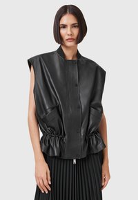 Black leather sleeveless jacket with a ribbed front, elastic cinched waist, and two side pockets. Smooth texture and tailored fit.