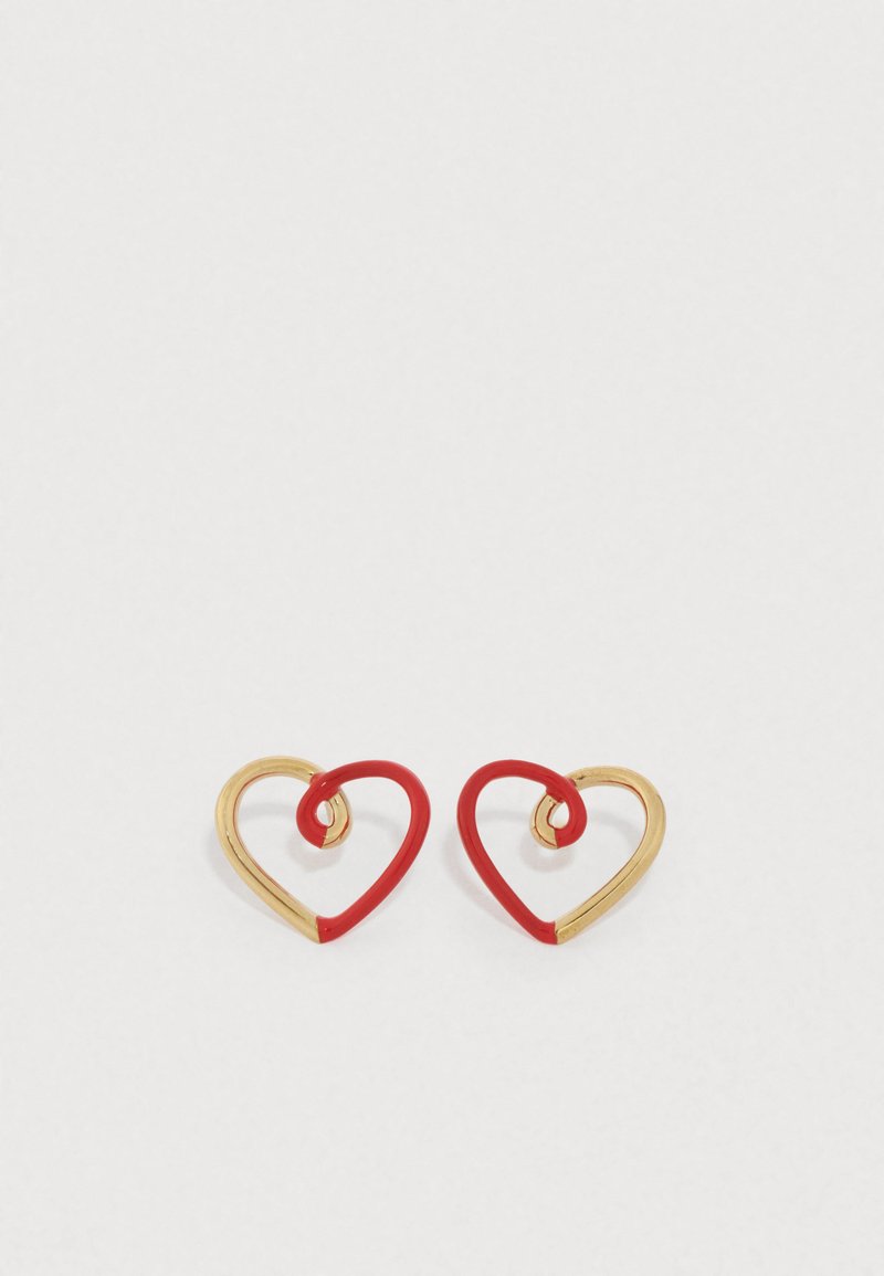 Auksinio tono metaliniai auskarai širdies formos su raudonos emalės akcentais; širdies formos viduje yra sukimo raštas.