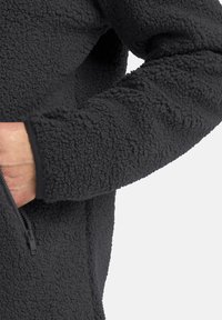 Schwarze Fleecejacke mit einer strukturierten, weichen Oberfläche. Verfügt über eine Reißverschlusstasche und elastische Bündchen für eine enge Passform.