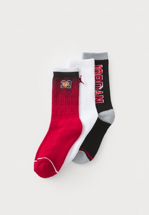 Tre calze sportive: una rossa con sfumature nere, una bianca con dettagli grigi e una nera con accenti rossi e testo.