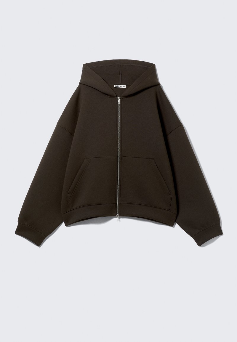 Sweat à capuche zippé marron foncé avec poches avant et large capuche, présenté sur un fond gris clair uni.