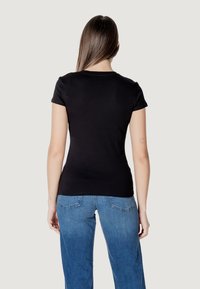 T-shirt nero a maniche corte con un design aderente. Materiale in cotone morbido. Indossato con jeans blu, mostrando uno stile classico e informale.