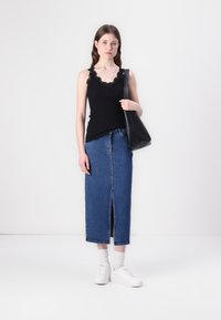 Svart ribbet tanktopp med blonder trim, kombinert med et denimskjørt med splitt foran, og hvite sneakers med ankelsokker. Svart tote bag inkludert.