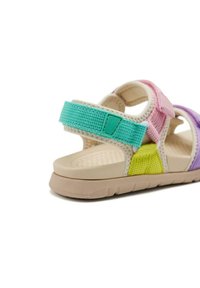 Sanda moderna multicolor con una suela de goma texturizada. Presenta correas ajustables de material trenzado en rosa, verde, amarillo y púrpura.