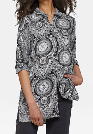 Camicia a maniche lunghe bianca e nera con colletto, caratterizzata da motivi circolari e un taglio comodo, abbinata a jeans scuri.