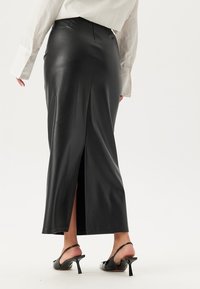 Zwarte leren maxi-rok met een zijsplit, gladde textuur, aansluitend ontwerp, gecombineerd met zwarte sandalen met hakken en bandjes.