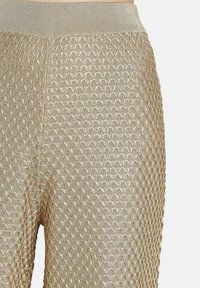 Gros plan sur un pantalon texturé marron doré avec un motif en losanges en relief et une taille élastique.