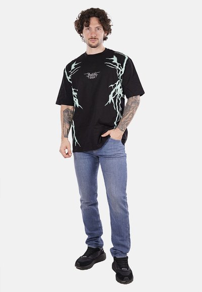 T-shirt nera oversize con grafiche a saetta blu chiaro, maniche corte e collo rotondo. Indossata con jeans blu chiaro e sneakers nere.